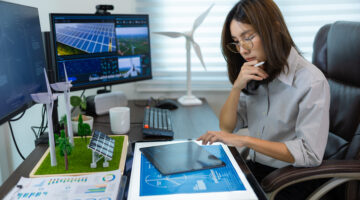 Portrait of a female engineer working with computer, wind turbine solar panel model for development of sustainable energy project.